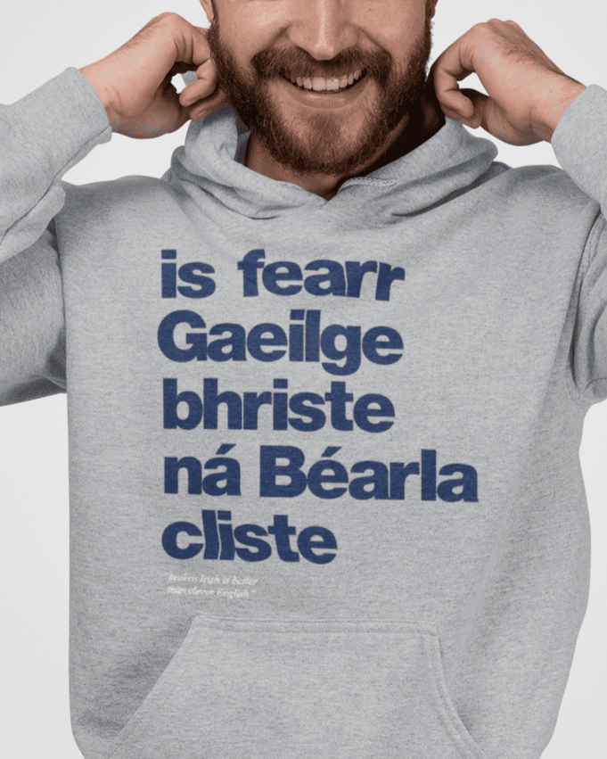 A person wearing a gray hoodie with the Irish phrase 'is fearr Gaeilge bhriste ná Béarla cliste' printed on it.
